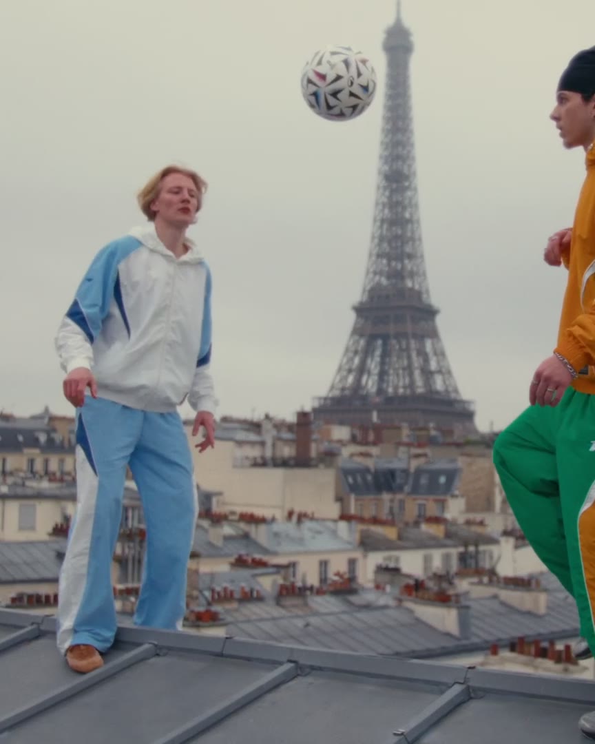 Two friends keeping a ball in the air on a zinc rooftop, the Eiffel Tower behind them